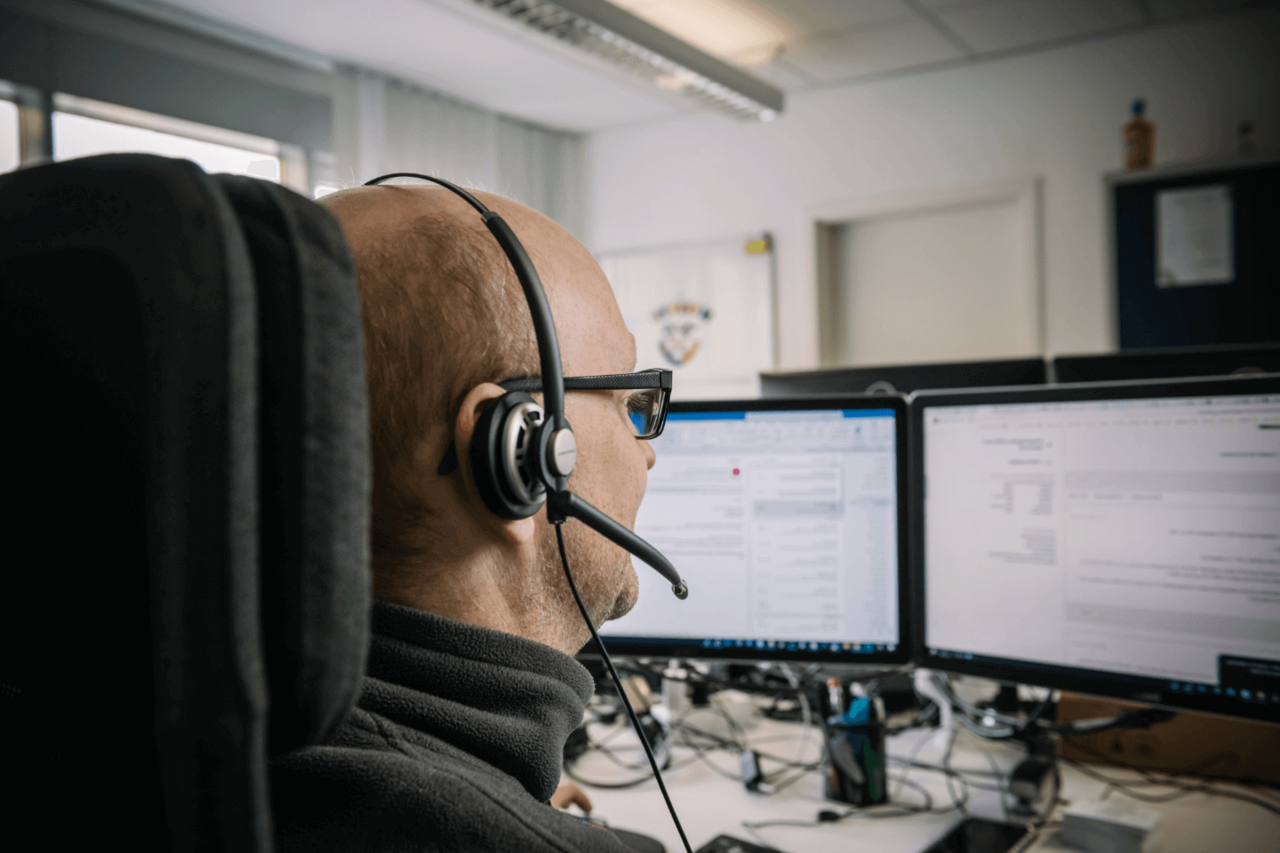 Support-Mitarbeiter mit Headset dokumentiert Vorgänge an zwei Monitoren